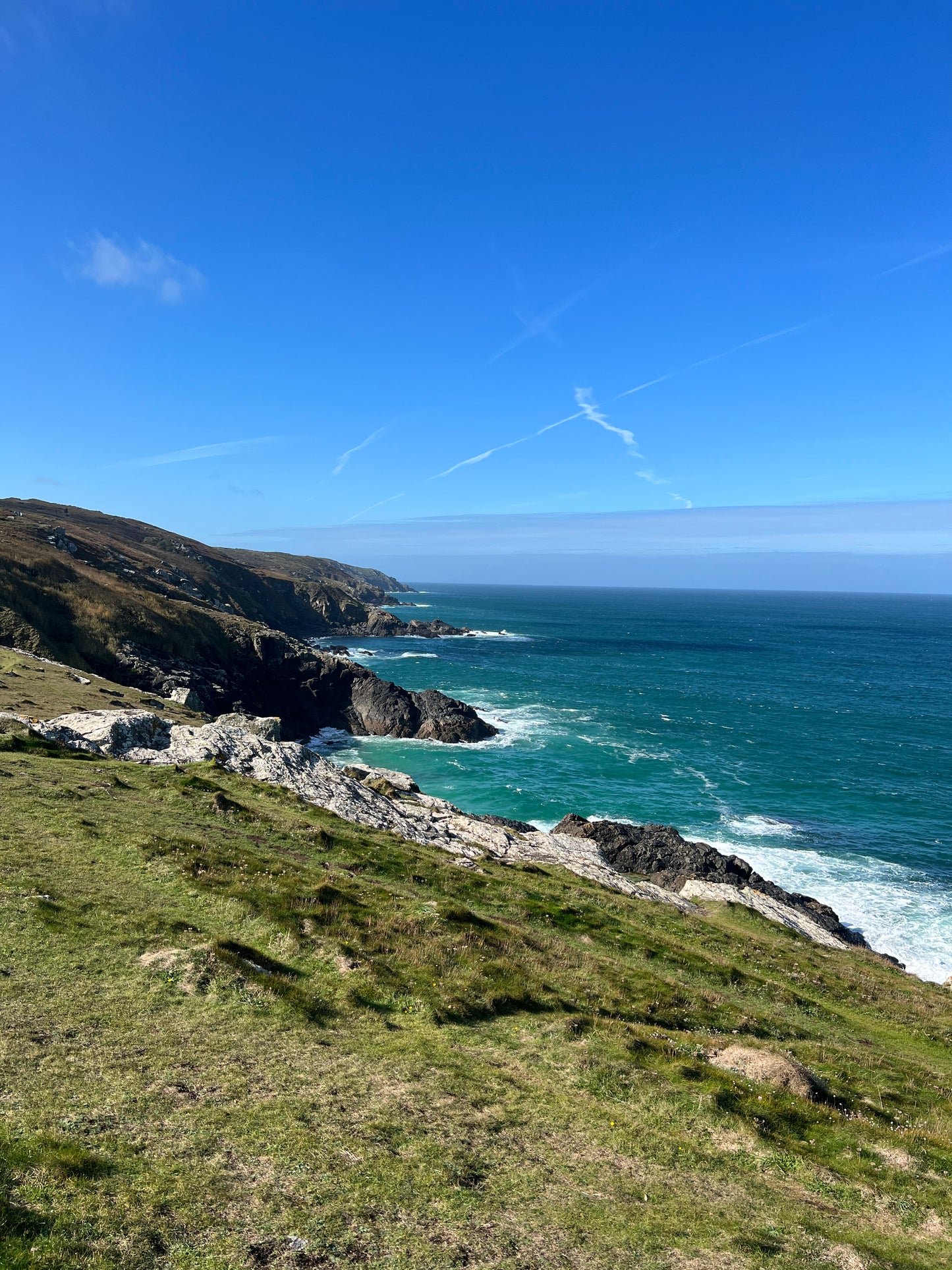 Coastline with grassy hill and ocean under a clear blue sky. St Ives, Cornwall.
