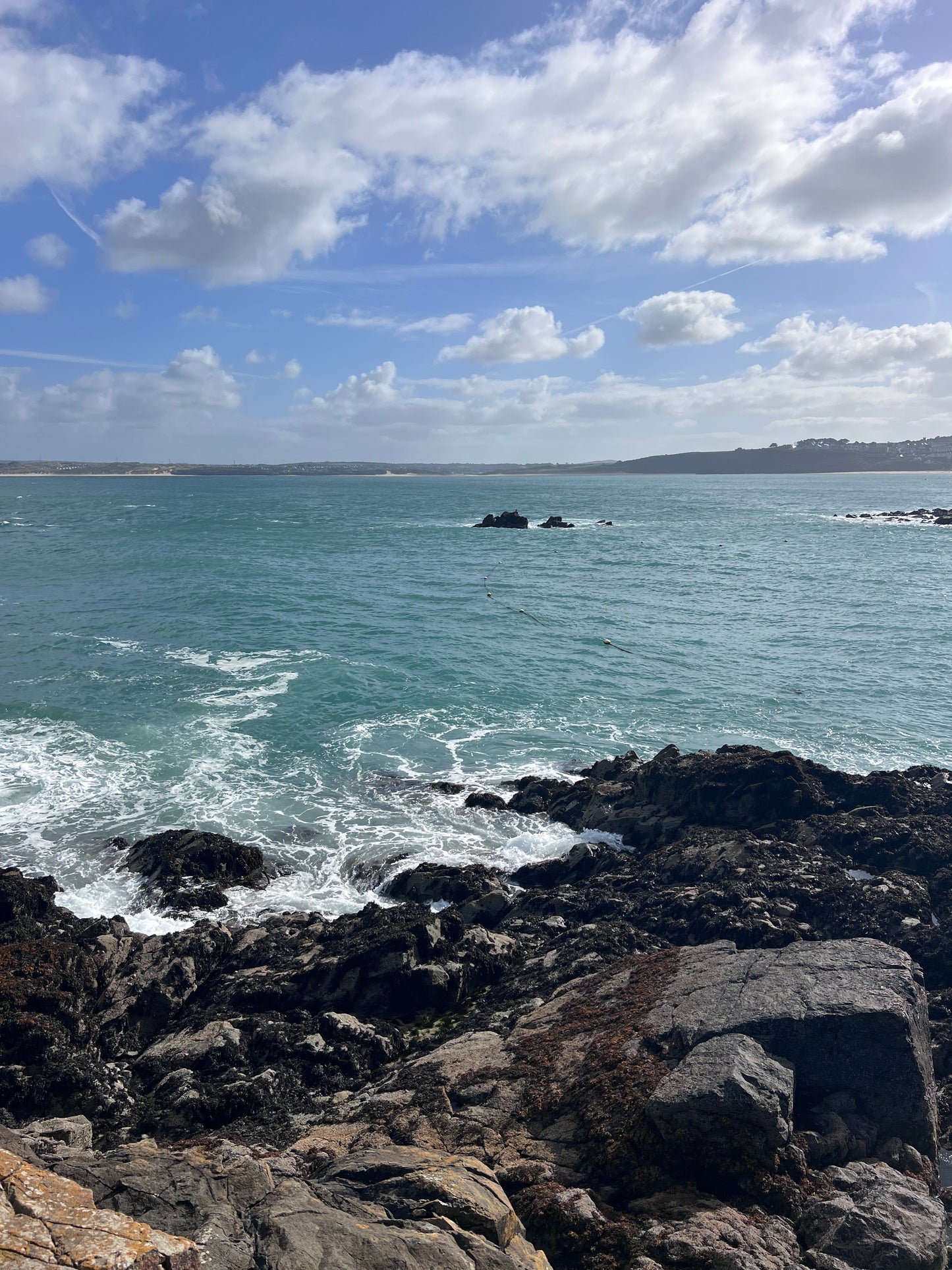 Rugged coastline with waves crashing against rocks under a partly cloudy sky. St Ives, Cornwall. Shem Hake Jewellery.