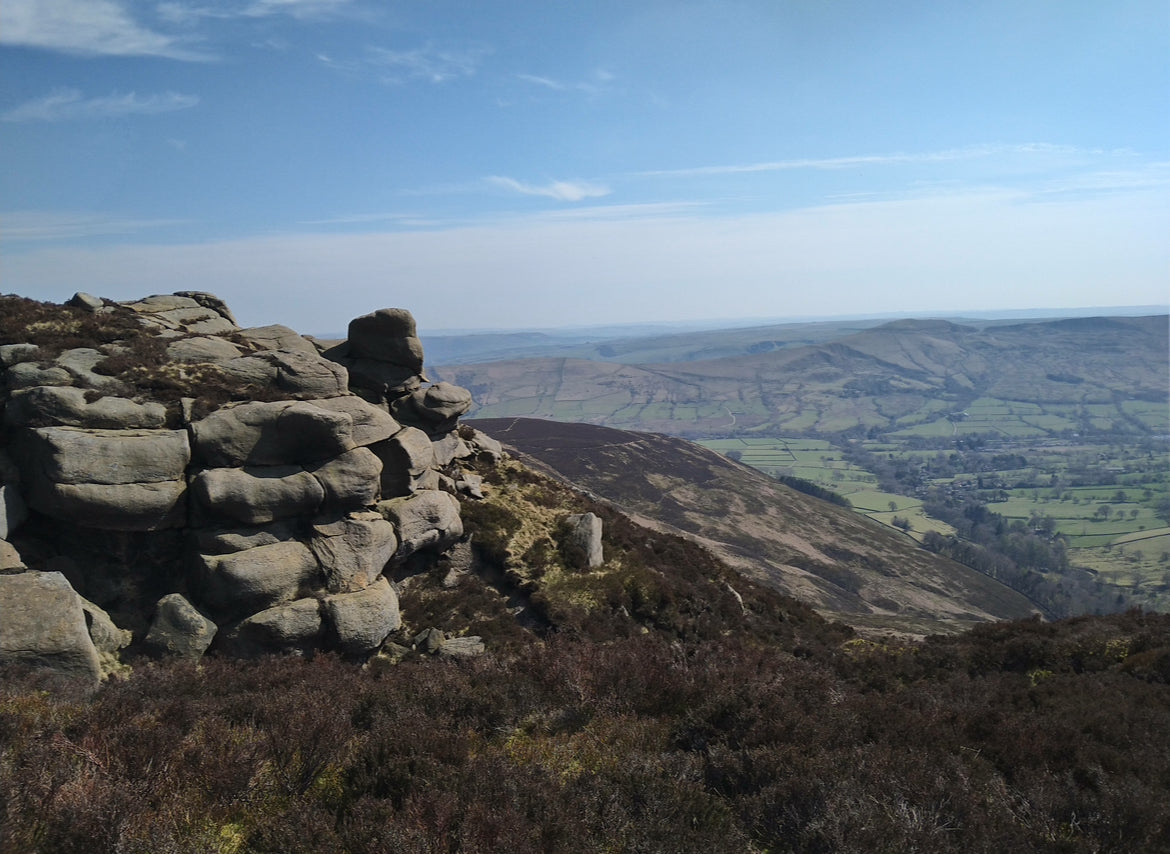 Rugged landscape with rocky outcrop and expansive view of a valley under a blue sky. Jewellery made in the Peak District.