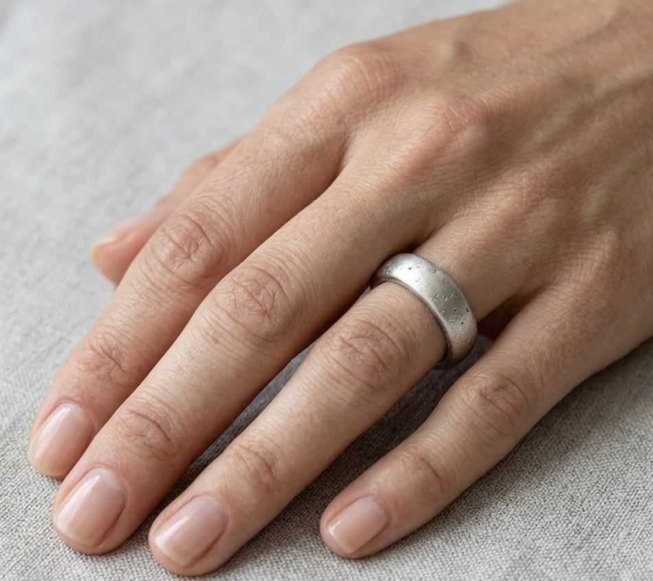 Hand wearing a white gold ring on a light fabric background. White gold ring made outdoors in Cornwall.