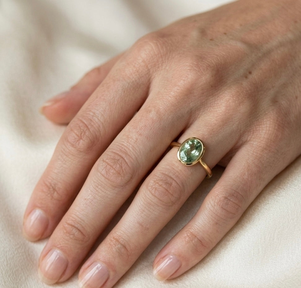 Hand wearing a gold ring with a green gemstone on a beige background