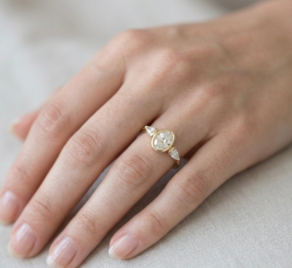 Gold ring with a diamond on a person's finger against a neutral background