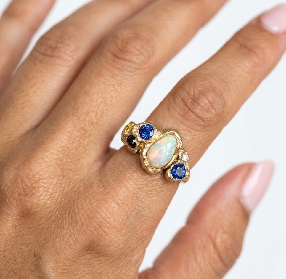 Gold ring with opal and sapphire stones on a hand against a white background