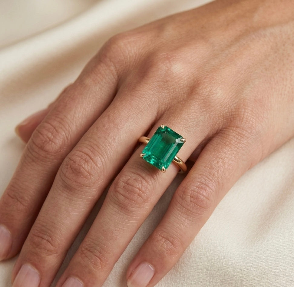 Hand wearing a gold ring with a green gemstone on a light background