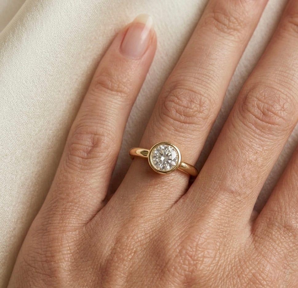 Gold ring with a diamond on a hand against a beige background