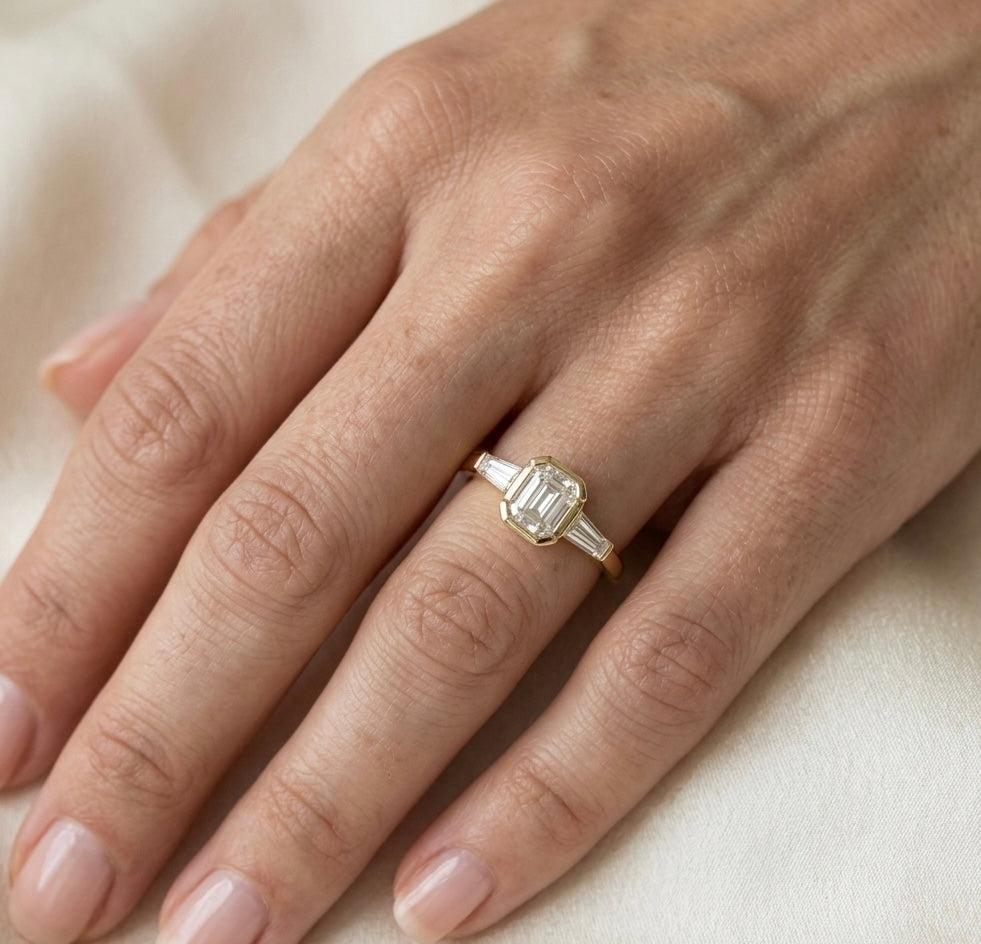 Gold ring with a diamond on a person's finger against a neutral background
