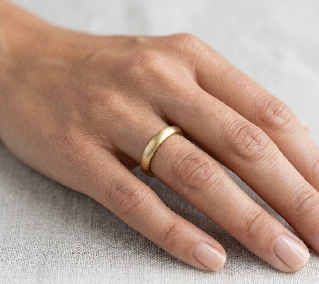 Hand wearing a gold ring on a light fabric background. Gold ring cast and made in St Ives, Cornwall in nature. Shem Hake Jewellery. 